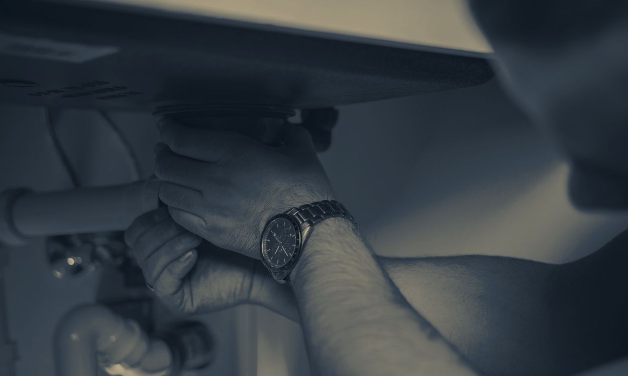Plumber's hands tightening a fitting under a sink